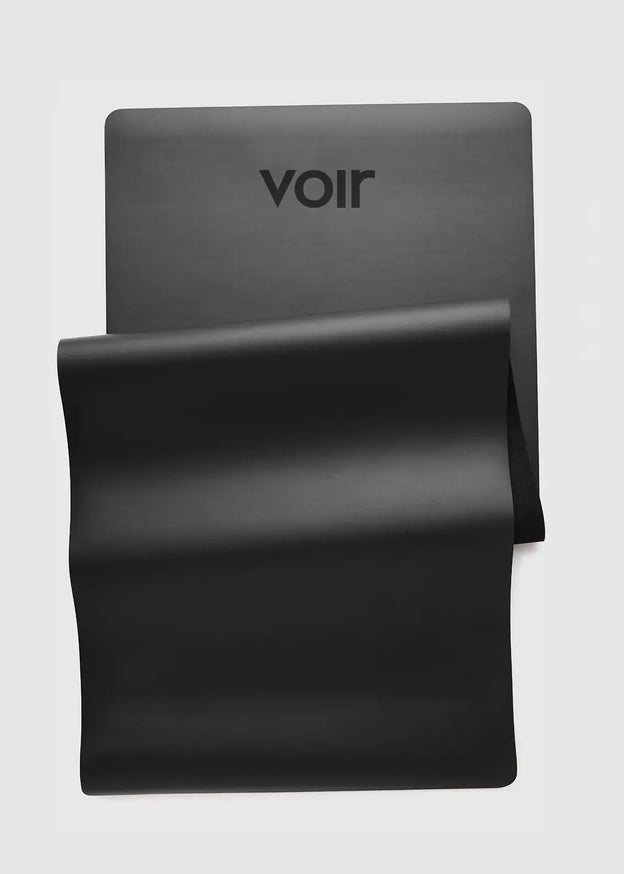 Mat de yoga y pilates VOIR Essential en negro, enrollado sobre fondo neutro - BLACK