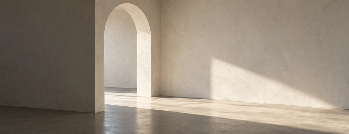Interior blanco con un arco y luz natural sobre el piso de concreto