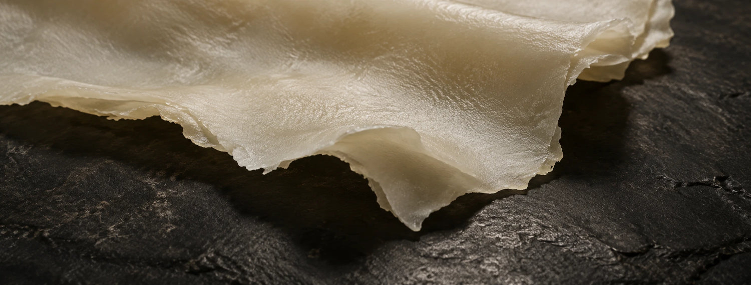 Lámina de caucho natural crudo, color crema y traslucida, sobre piedra oscura