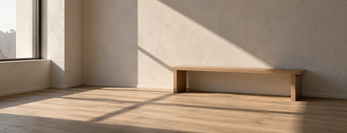 Rincón de un estudio vacío con muro de estuco claro, piso de madera y un banco bajo